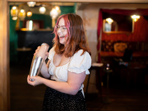 A woman laughs while learning how to shake cocktails